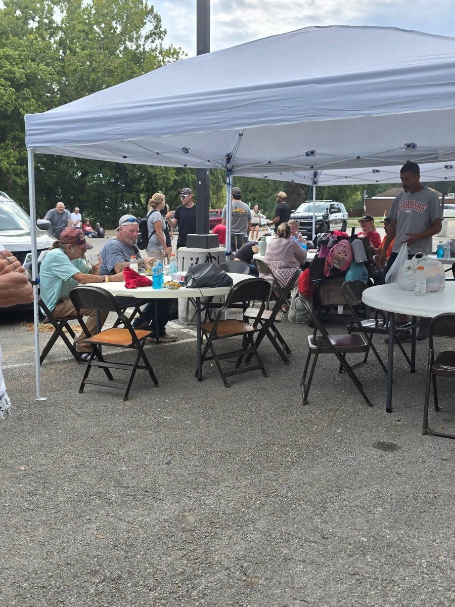 Neighbors sitting together at tables under a canopy, sharing a meal